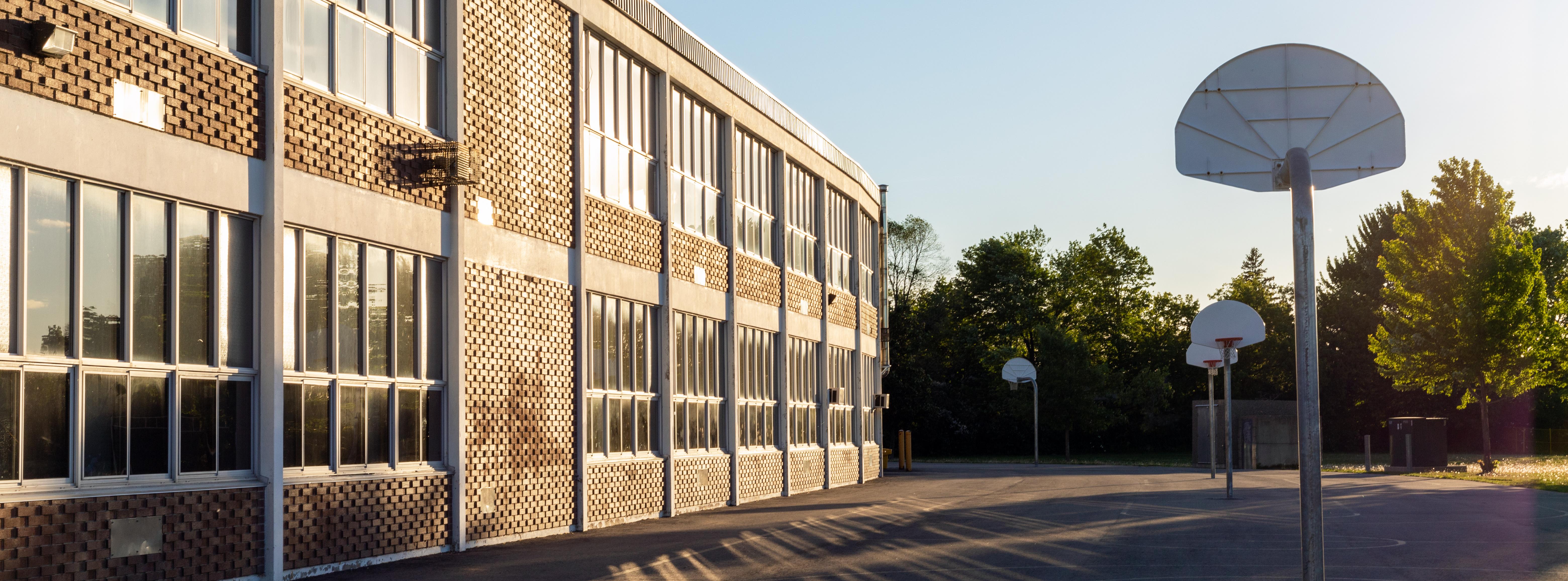 Schulgebäude und Schulhof mit Basketballkörben in der Abendsonne