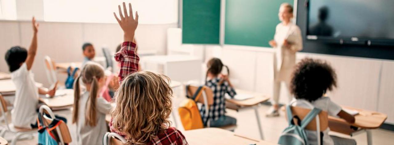 Schulkinder im Unterricht mit Lehrerin im Hintergrund