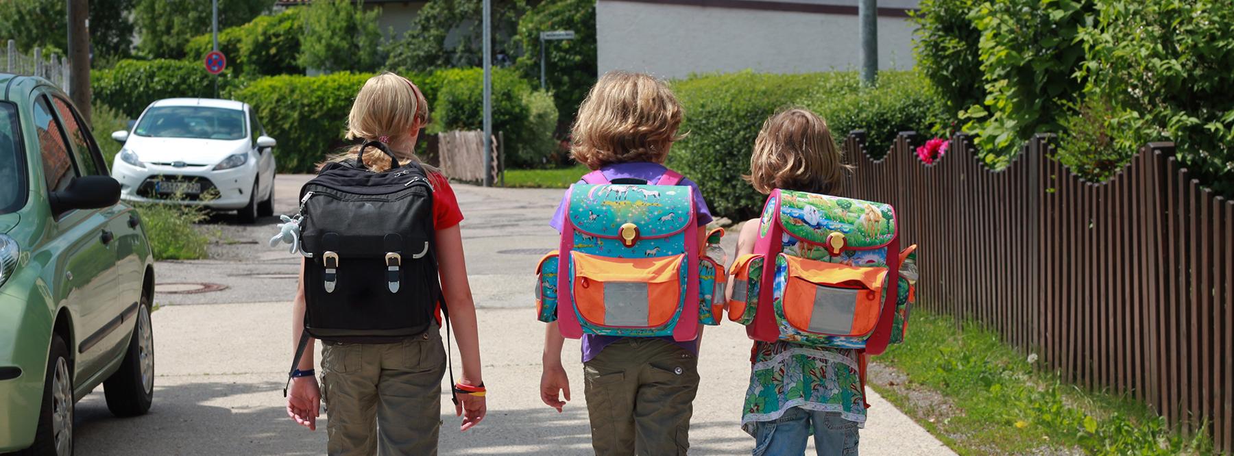 Drei Kinder mit Schulranzen sind auf dem Schulweg.
