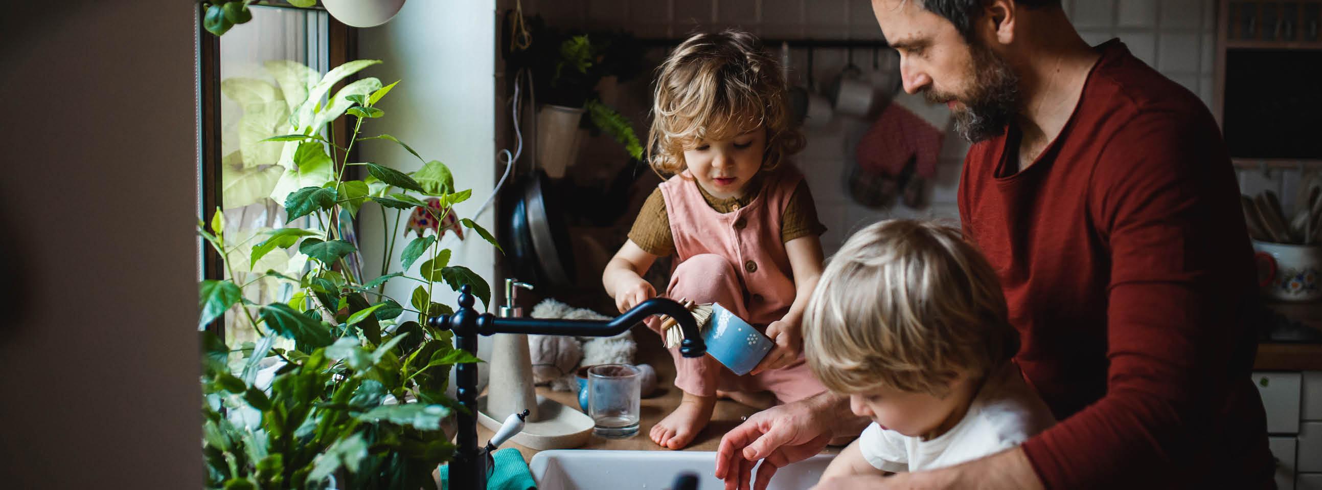 Vater mit zwei Kleinkindern beim Spülen in der Küche