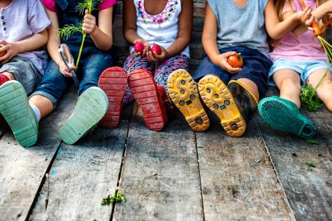 Kinder, die nebeneinander sitzen und Gemüse in der halten. 