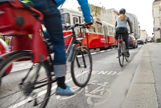 Gefährliche Begegnung zwischen Radfahrern, Autos und einer Straßenbahn am Ende eines markierten Radwegs auf einer stark befahrenen Straße.