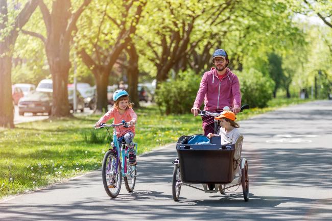 Das Bild zeigt einen Vater mit zwei Kindern beim Fahrradfahren. 