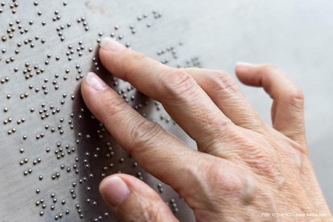 Das Bild zeigt eine Hand, die über Brailleschrift geht. 