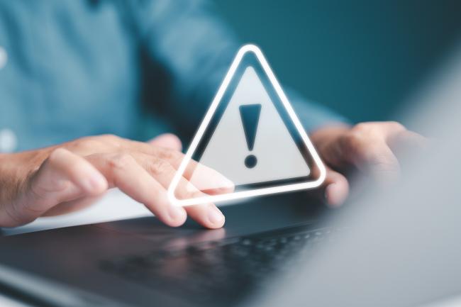 Person tippt am Laptop, Warnhinweis mit Ausrufezeichen