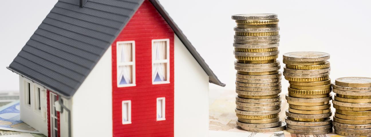 Das Bild zeigt ein Miniaturhaus, daneben Münzen und Euro-Scheine 