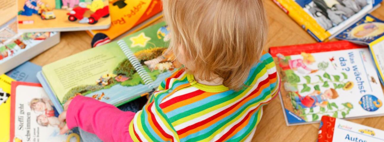 Ein Kind sitzt auf dem Boden und schaut sich Bilderbücher an.