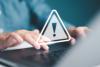 Person tippt am Laptop, Warnhinweis mit Ausrufezeichen
