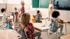 Schulkinder im Unterricht mit Lehrerin im Hintergrund